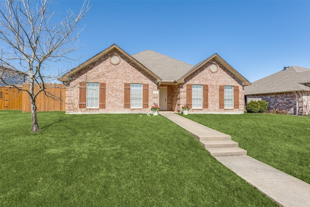 single story home featuring a front yard, fence, brick siding, and a shingled roof