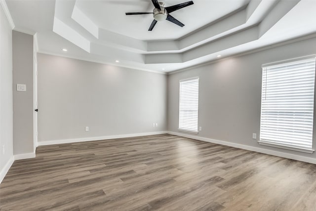 empty room featuring ornamental molding, a tray ceiling, wood finished floors, baseboards, and ceiling fan