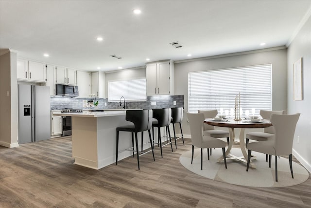 kitchen featuring visible vents, crown molding, decorative backsplash, appliances with stainless steel finishes, and wood finished floors