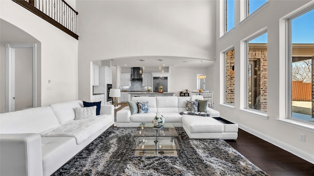 living room featuring dark wood-style flooring, a towering ceiling, and baseboards