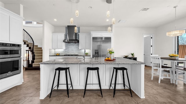 kitchen with stainless steel appliances, visible vents, wall chimney range hood, and a kitchen bar