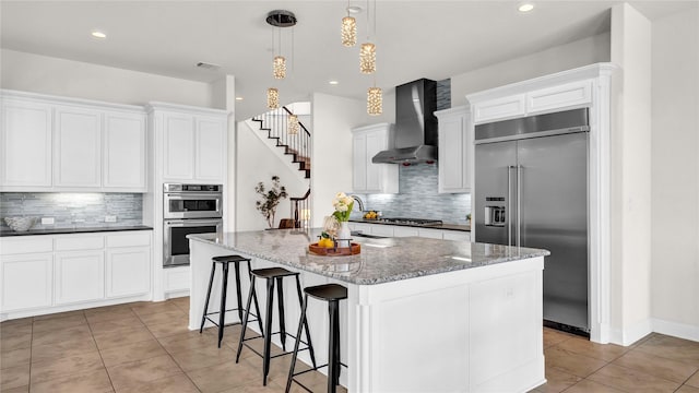 kitchen featuring light tile patterned floors, visible vents, wall chimney exhaust hood, a kitchen island with sink, and stainless steel appliances