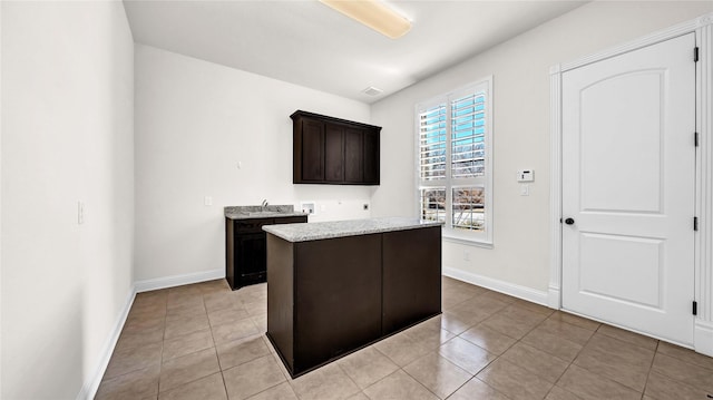 kitchen featuring a kitchen island, dark brown cabinetry, light stone counters, and baseboards