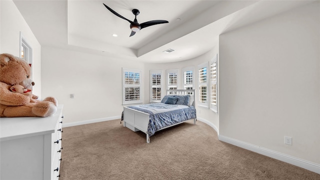 carpeted bedroom with baseboards, visible vents, a tray ceiling, and ceiling fan