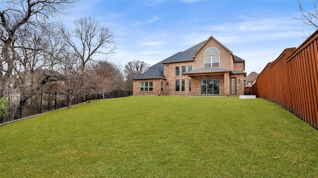 back of house with a fenced backyard, a yard, brick siding, and roof with shingles