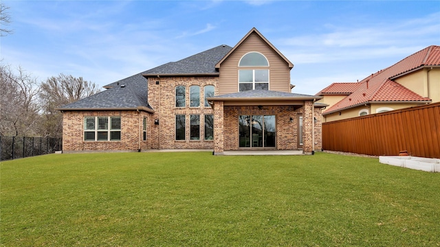 back of house with brick siding, a fenced backyard, roof with shingles, and a yard