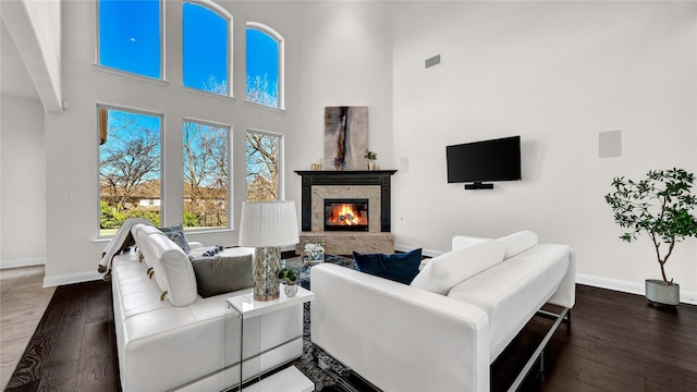 living room featuring hardwood / wood-style flooring, baseboards, visible vents, and a stone fireplace