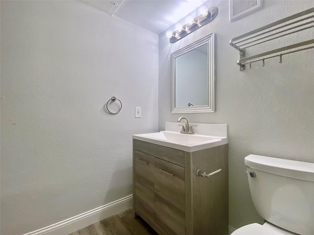 bathroom with toilet, wood finished floors, visible vents, vanity, and baseboards