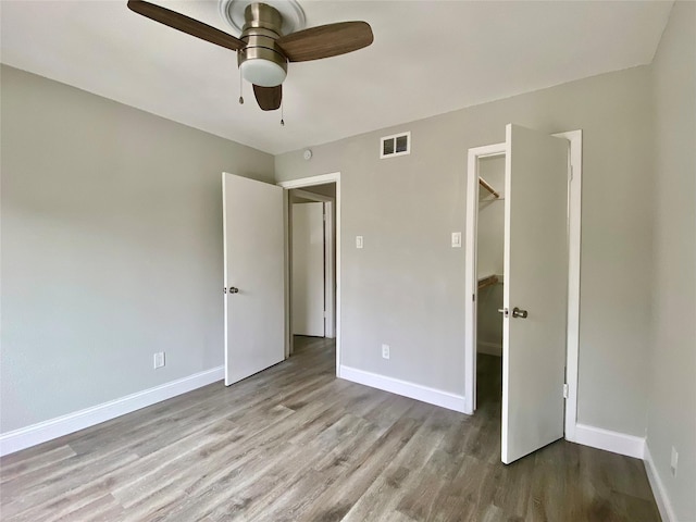 unfurnished bedroom with a spacious closet, wood finished floors, visible vents, and baseboards