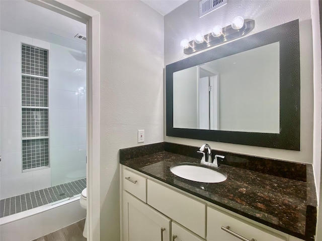 full bathroom featuring a textured wall, toilet, visible vents, vanity, and a tile shower