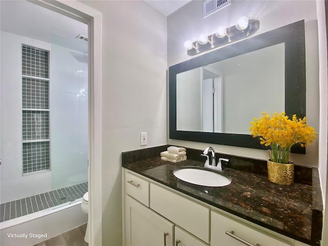 full bathroom with visible vents, vanity, toilet, and tiled shower