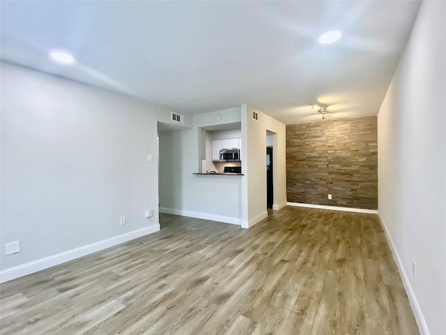 unfurnished living room with an accent wall, light wood-type flooring, visible vents, and baseboards