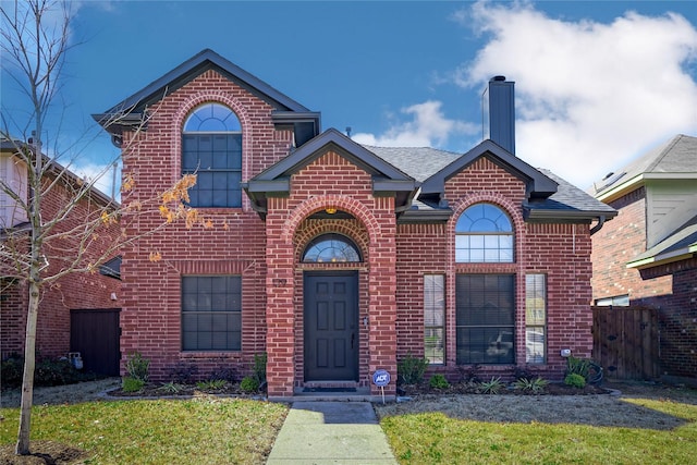 traditional-style house featuring brick siding, fence, a chimney, and roof with shingles