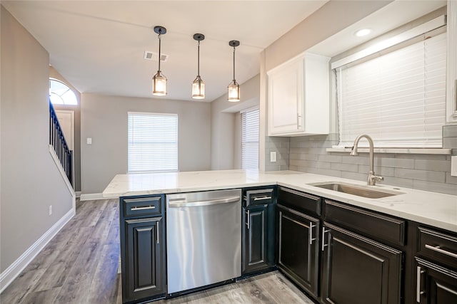 kitchen featuring light wood finished floors, tasteful backsplash, stainless steel dishwasher, white cabinets, and a sink