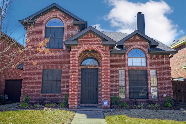 traditional home featuring roof with shingles, brick siding, a chimney, and fence