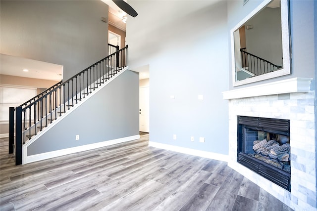 unfurnished living room featuring a high ceiling, wood finished floors, baseboards, stairway, and a glass covered fireplace