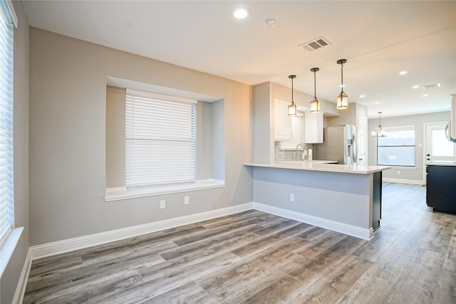 kitchen with stainless steel refrigerator with ice dispenser, light countertops, visible vents, wood finished floors, and baseboards