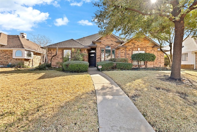 ranch-style house with brick siding, a front yard, and a shingled roof