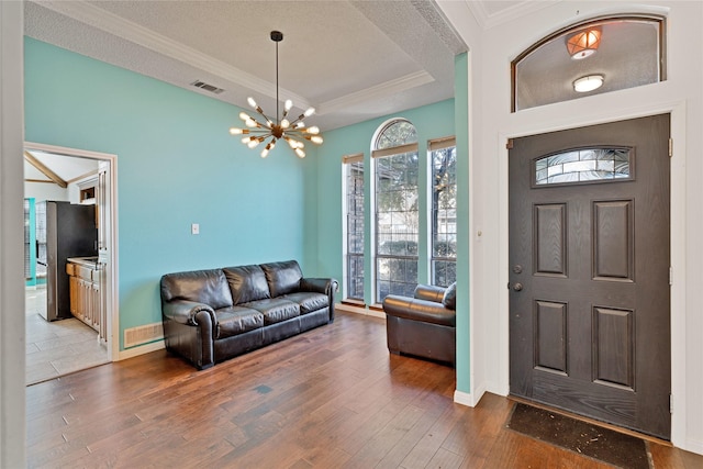 entrance foyer with visible vents, a raised ceiling, wood finished floors, crown molding, and a notable chandelier