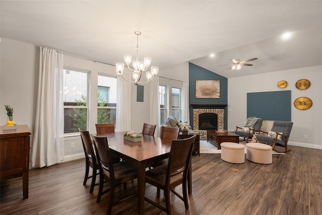 dining room featuring ceiling fan with notable chandelier, dark wood-type flooring, a fireplace, baseboards, and vaulted ceiling