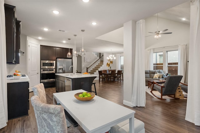 kitchen with appliances with stainless steel finishes, a kitchen island with sink, a kitchen breakfast bar, and dark wood-style floors