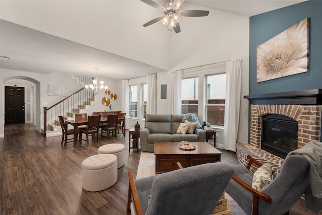 living room with arched walkways, dark wood-style flooring, stairway, a brick fireplace, and ceiling fan with notable chandelier