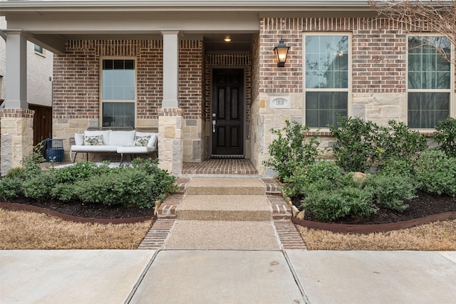 doorway to property with an outdoor hangout area, stone siding, brick siding, and a porch