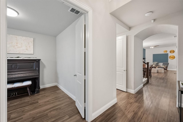 hall featuring baseboards, visible vents, arched walkways, and wood finished floors