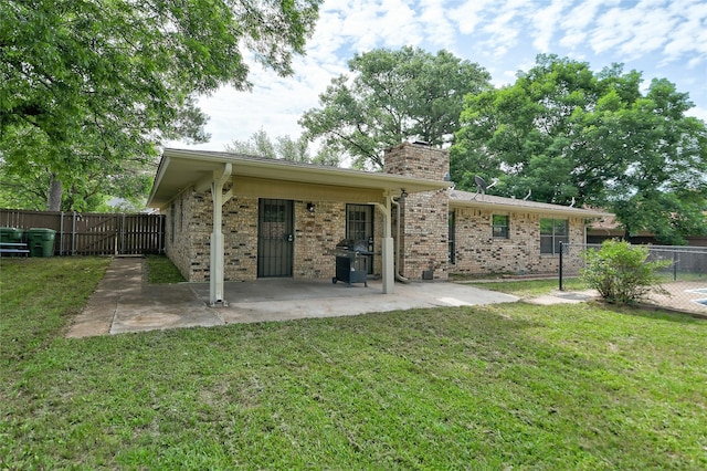 rear view of property with brick siding, a yard, a chimney, a patio area, and fence