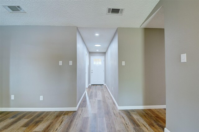 hall with visible vents, a textured ceiling, and wood finished floors