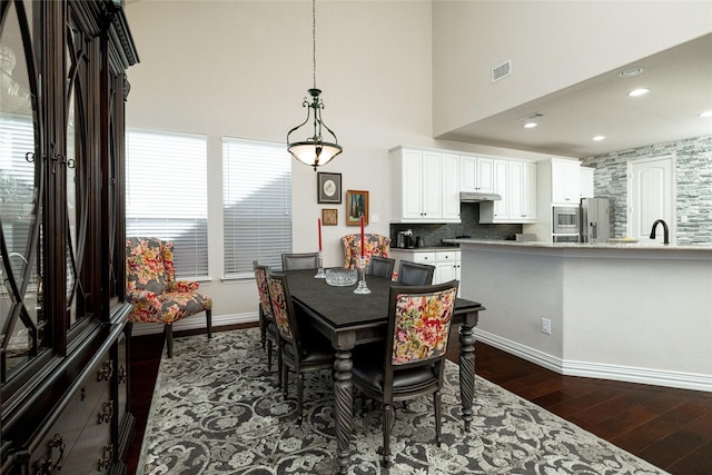 dining area featuring dark wood finished floors, a high ceiling, baseboards, and visible vents