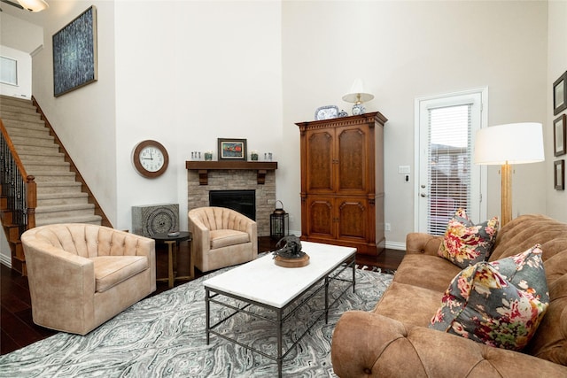 living area featuring wood finished floors, stairway, a high ceiling, a stone fireplace, and baseboards