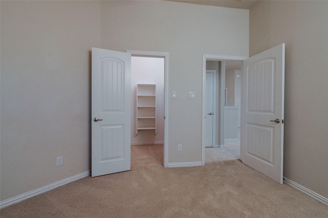 unfurnished bedroom featuring a closet, carpet flooring, baseboards, a towering ceiling, and a spacious closet