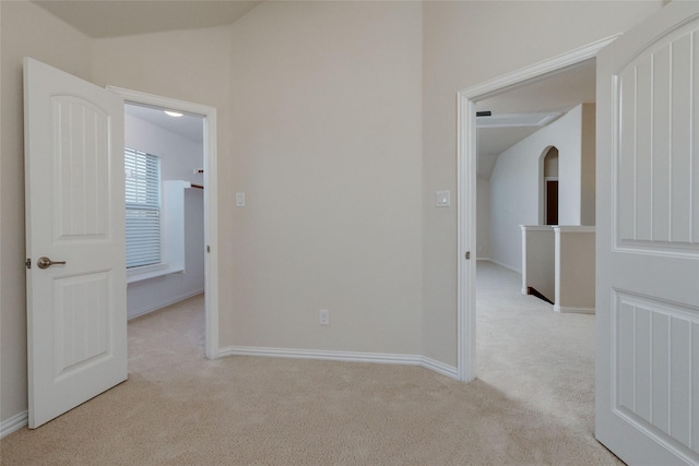 spare room featuring baseboards, light carpet, arched walkways, and lofted ceiling