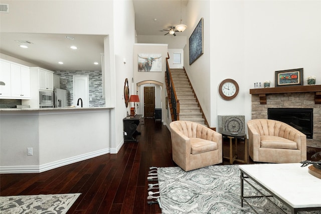 living room featuring visible vents, stairway, wood-type flooring, a high ceiling, and a stone fireplace