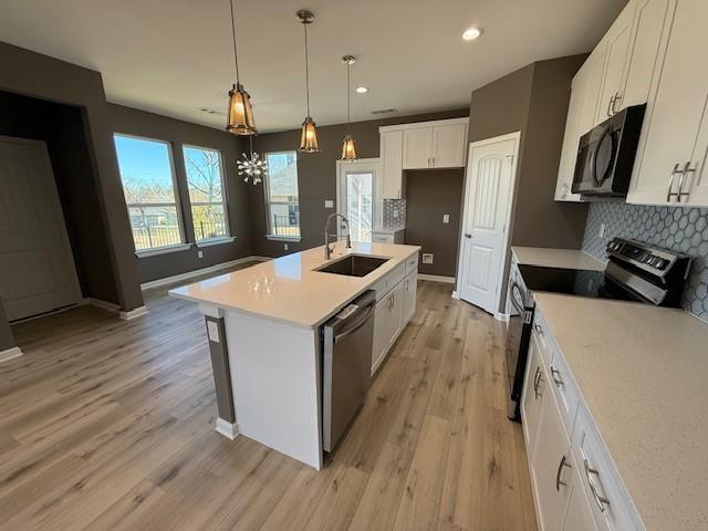 kitchen featuring light countertops, appliances with stainless steel finishes, light wood-style floors, white cabinetry, and a sink