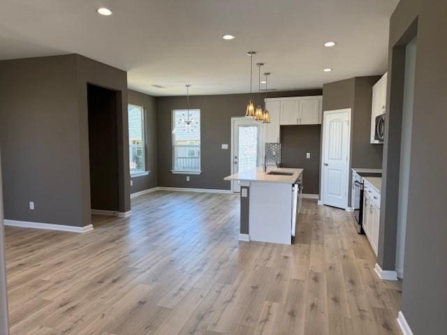 kitchen featuring baseboards, white cabinets, open floor plan, stainless steel appliances, and a sink