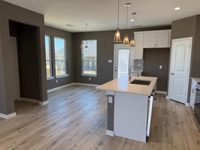 kitchen featuring light wood finished floors, light countertops, white cabinets, a sink, and baseboards