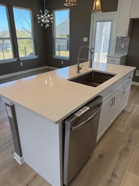 kitchen with a notable chandelier, dishwasher, light wood-style flooring, and a sink