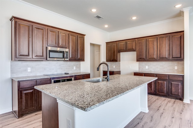 kitchen with visible vents, light wood-style flooring, stainless steel microwave, light stone countertops, and a sink