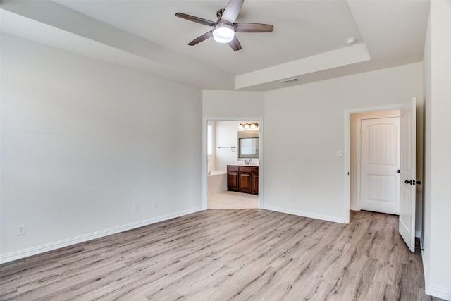 unfurnished bedroom with light wood finished floors, a tray ceiling, visible vents, and baseboards