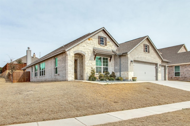 french country home featuring brick siding, fence, driveway, roof with shingles, and a chimney