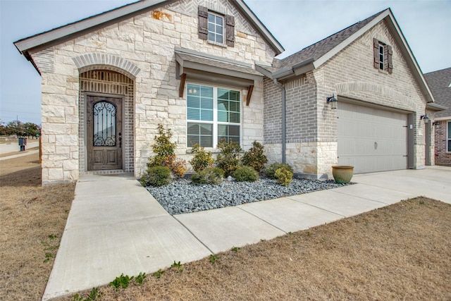 view of front of home featuring driveway, stone siding, roof with shingles, an attached garage, and brick siding