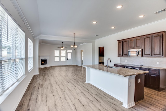 kitchen featuring a fireplace with raised hearth, a sink, visible vents, backsplash, and stainless steel microwave