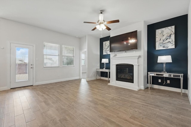 unfurnished living room featuring a glass covered fireplace, ceiling fan, baseboards, and wood finished floors