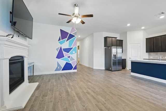 unfurnished living room with light wood finished floors, ceiling fan, visible vents, and a glass covered fireplace