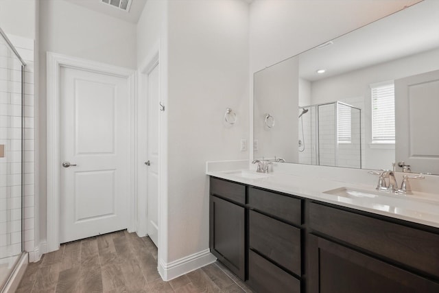 full bath featuring double vanity, a sink, a shower stall, and wood finished floors