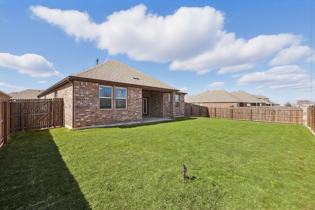 back of house featuring brick siding, roof with shingles, a lawn, a patio area, and a fenced backyard