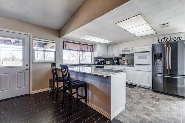 kitchen featuring a warming drawer, visible vents, white cabinets, a sink, and white appliances