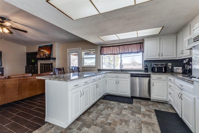 kitchen with a peninsula, a fireplace, a sink, white cabinets, and stainless steel dishwasher